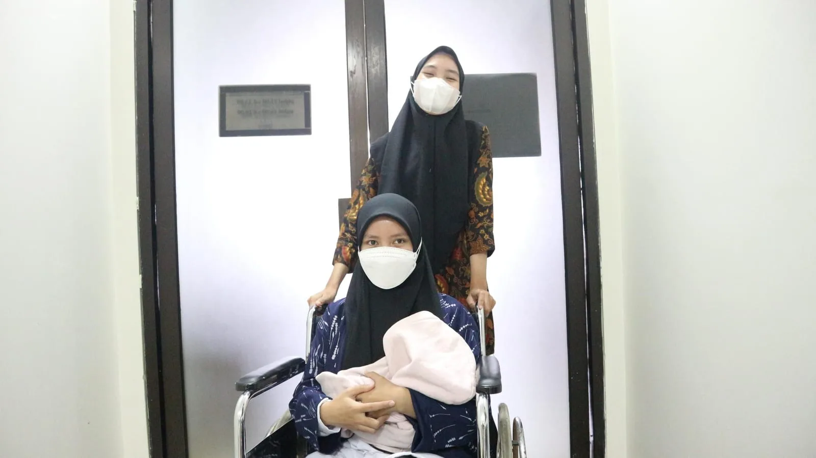 Seorang ibu duduk di kursi roda sambil menggendong bayinya, didorong oleh petugas RS Anggrek Mas saat akan meninggalkan ruang perawatan.