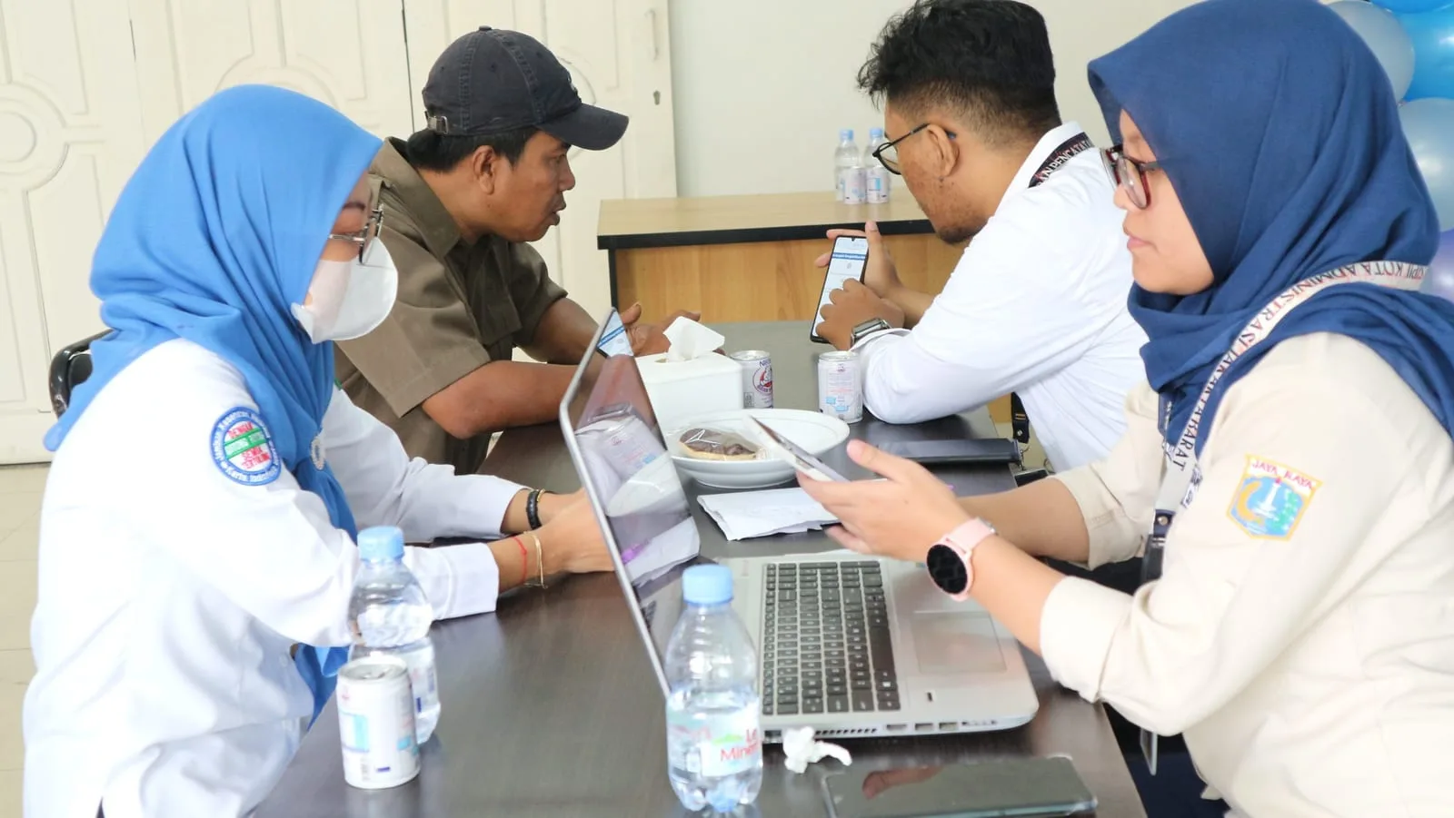 Petugas berseragam melayani warga di meja layanan aktivasi KTP digital di RS Anggrek Mas, dengan laptop dan telepon genggam di atas meja.