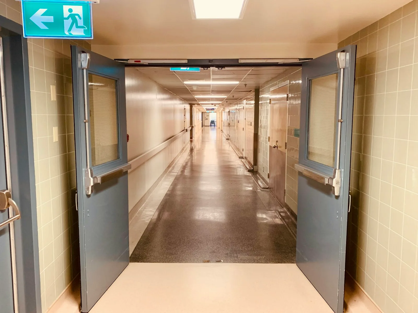 Lorong rumah sakit yang lengang dengan pintu ayun ganda di ujungnya.