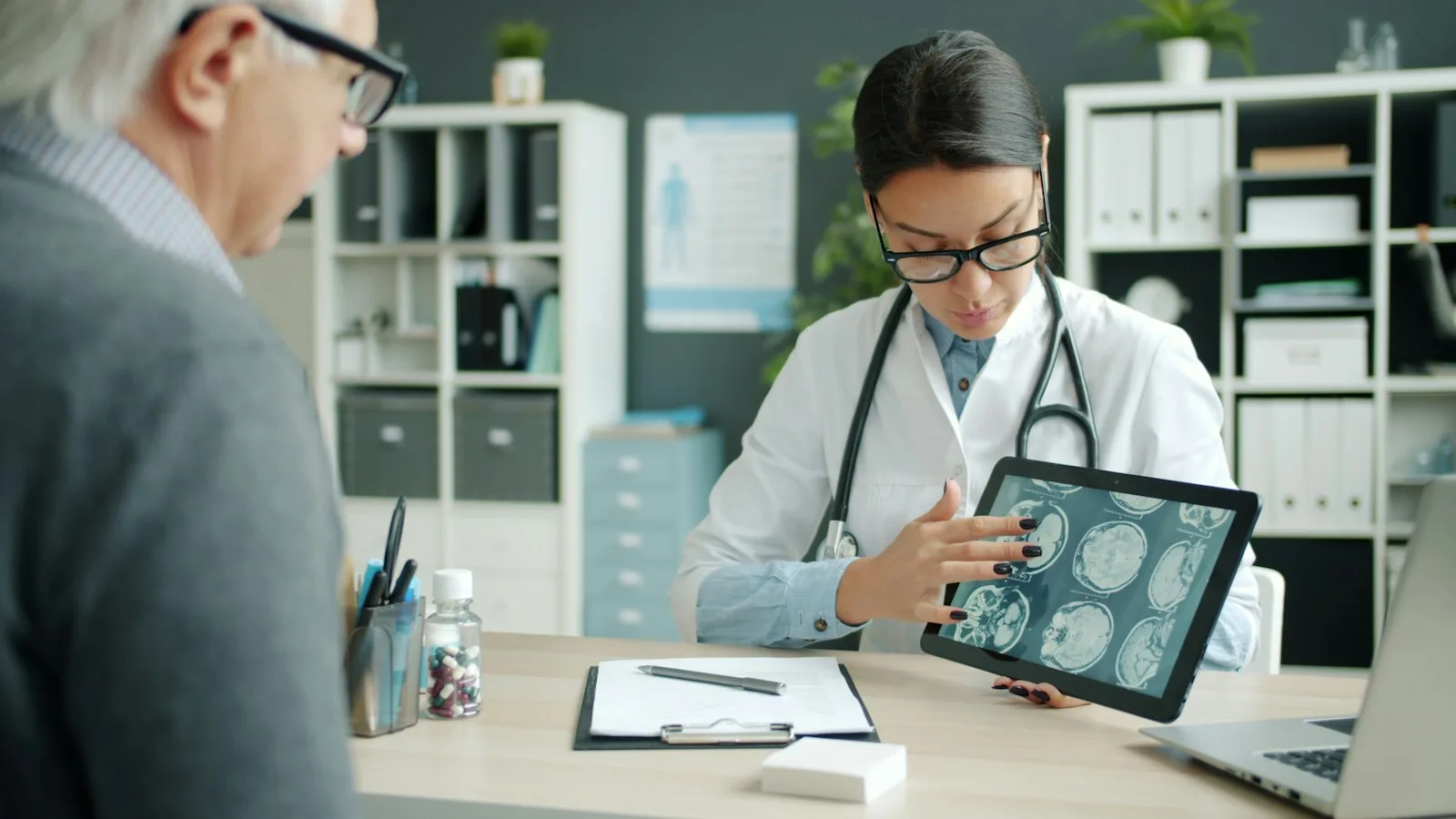 Seorang dokter perempuan mengamati hasil pencitraan otak pada layar tablet di ruang praktik.