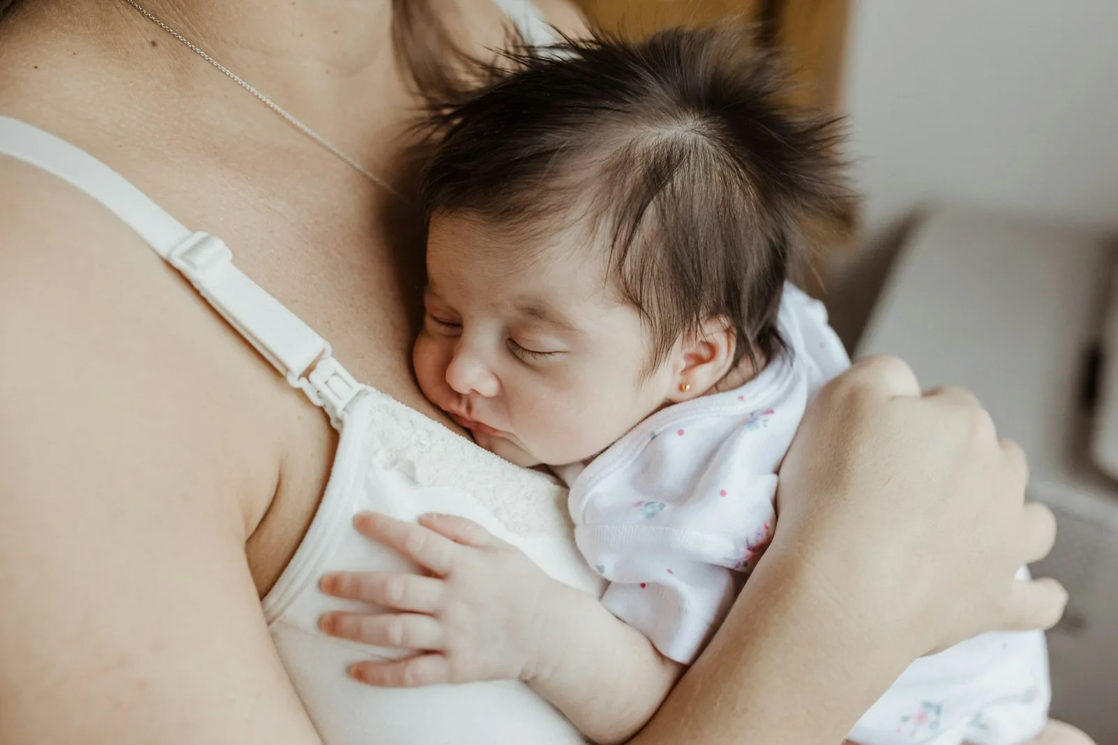 Bayi baru lahir tertidur di dada ibunya yang mengenakan atasan menyusui, tangan ibu menopang punggung bayi.